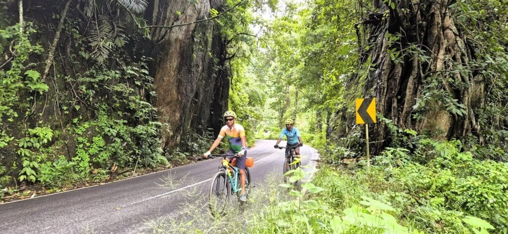 Two cyclists pedal down a offbeat path, surrounded by greenery on their journey to Munnar.