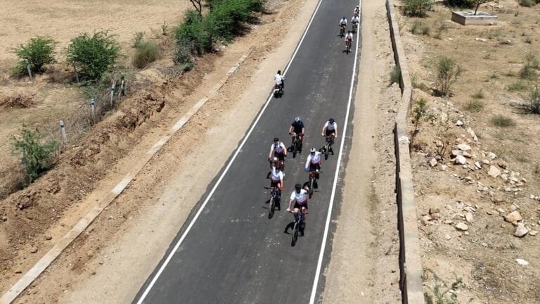 Cyclists riding through a picturesque rural landscape in Rajasthan, surrounded by fields.