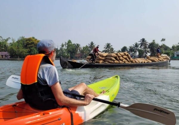 Kayaking in Nedumudi, Kerala, with kayakers paddling through the peaceful backwaters, surrounded by lush greenery and traditional village scenes.