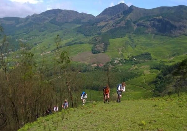 Trekking through the Western Ghats, Kerala, with hikers traversing rugged terrains, surrounded by misty hills and dense forests, experiencing the region's natural beauty.