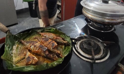 A man is cooking fish in a pan on a stove.