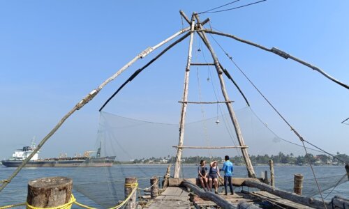 Fishermen at work near the beach in Fort Kochi, Kerala, using traditional Chinese fishing nets, with the distant view of the Arabian Sea adding to the coastal charm.