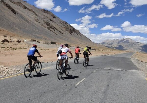 Cyclists navigate a winding road in the mountains near Manali, surrounded by the breathtaking Himalayan landscape.