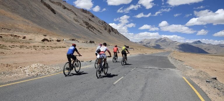 Cyclists navigate a winding road in the mountains near Manali, surrounded by the breathtaking Himalayan landscape.