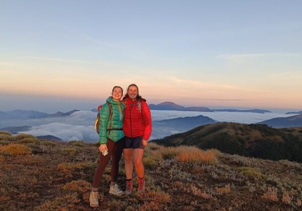 Two trekkers stand atop Meeshapulimala, enjoying stunning views of misty hills and valleys in the Western Ghats.