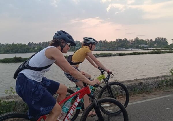 Two people cycling along a road beside fish farms in Cherai's rural village.