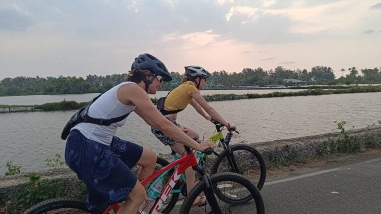 Two people cycling along a road beside fish farms in Cherai's rural village.