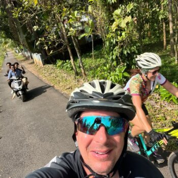 A cyclist navigating the scenic route from Kochi to Thattekad, with the road flanked by dense greenery and tall trees, offering a peaceful and refreshing cycling experience.