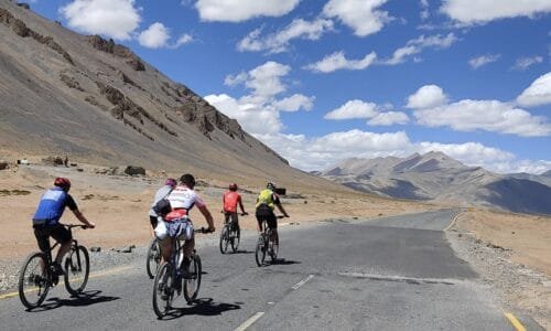 Three cyclists ride along a mountain road during the Manali to Leh cycling adventure.