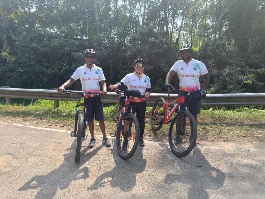 Three people stand by their bikes on a peaceful road in the Western Ghats foothills of Kerala.