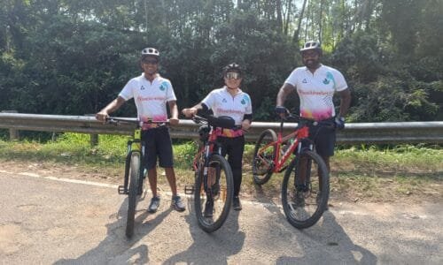 Three people stand by their bikes on a peaceful road in the Western Ghats foothills of Kerala.