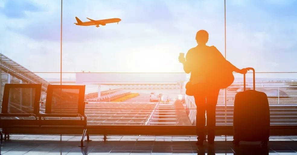 A traveler waits by a window with their luggage, anticipating their flight after an airport drop-off.