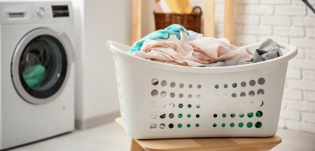 A basket of clothes on a stool beside a washing machine, ready for laundry day.