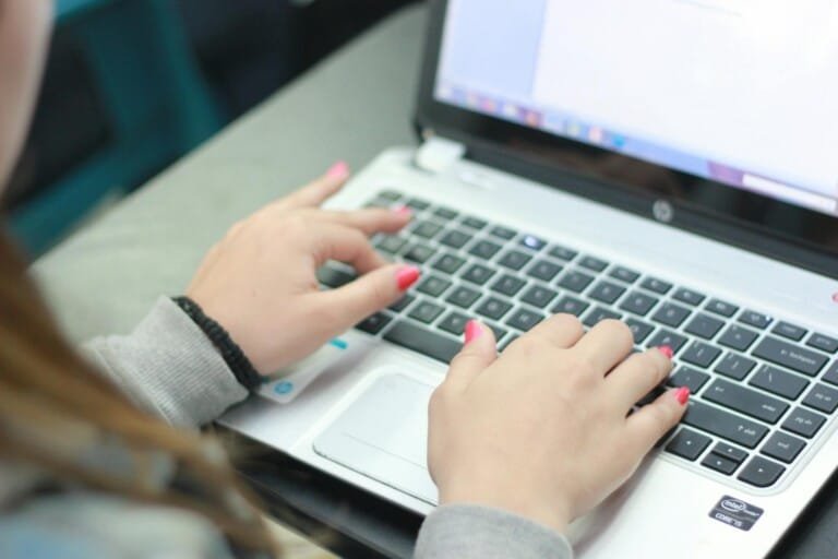 A woman focused on typing on her laptop, with a cozy workspace in the background.