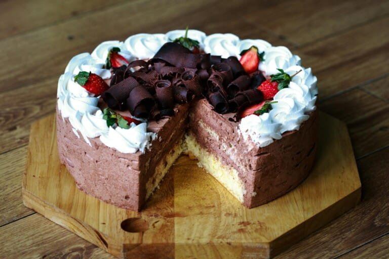 A rich chocolate cake topped with fresh strawberries and a swirl of whipped cream.