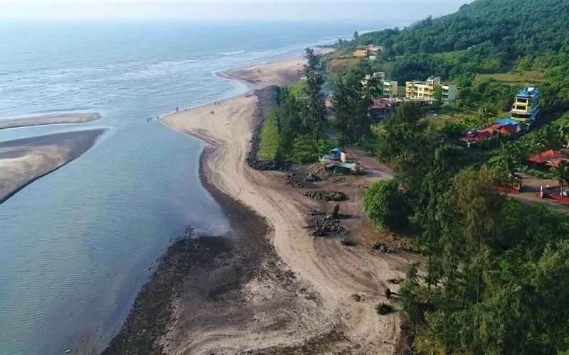35 Aerial view of a coastal tropical landscape with a long sandy beach, lush green vegetation, and buildings along the shoreline. The image shows the natural beauty of the coastal environment with the ocean in the background.